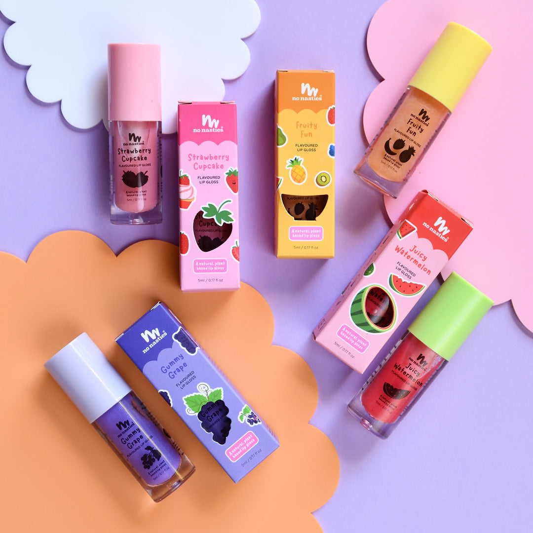 A collection of kids' lip glosses in various fruity flavors, displayed on a colorful background. The lip glosses are packaged in cardboard boxes with cut-outs, designed to look like fruit slices.