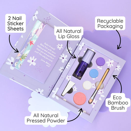 A boxed makeup set labeled 'mw no noodles DELUXE MAKEUP SET' lies on a lavender background with white paper flower cutouts around it. The box is light purple and white with a cartoon face illustration and a brown circular badge.