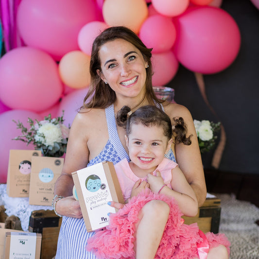 mum with brunette hair and little daughter sitting on her lap with pink balloons in the background