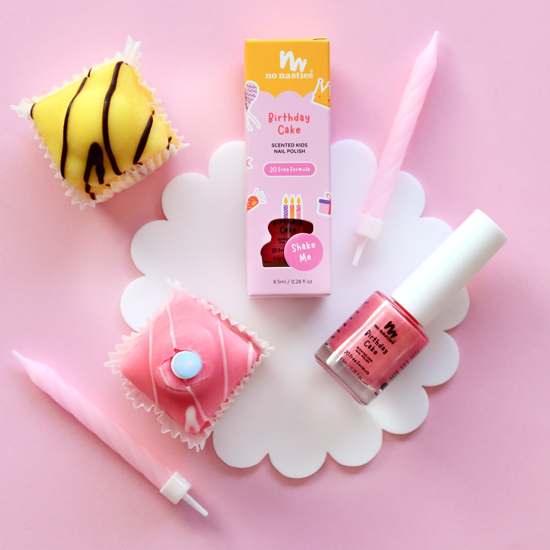 A bottle of kids' nail polish in party pink color, along with a cupcake decorated with a pink icing, and two other cupcakes with different toppings, presented on a pink background.