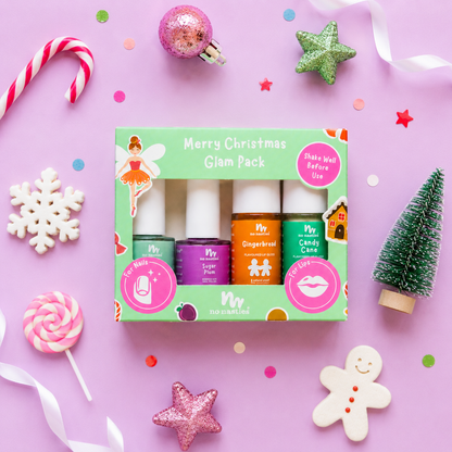 A flat-lay of a 'Merry Christmas Glam Pack' nail polish set by 'no touch nail care' on a light purple background decorated with festive holiday props like candy canes, a lollipop, and a gingerbread man.
