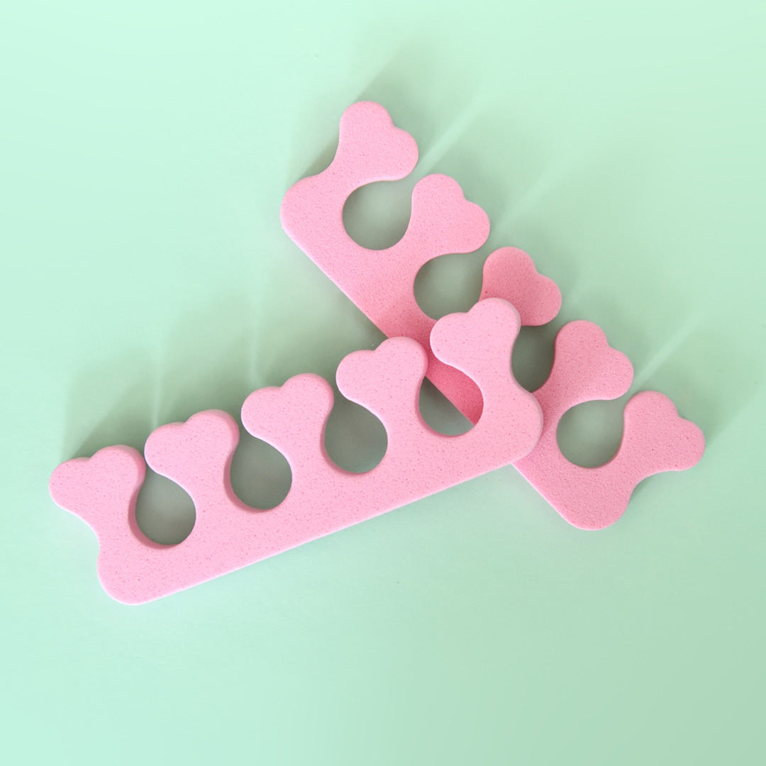 Two pink toe separators designed with heart shapes on the ends, placed on a light green background.