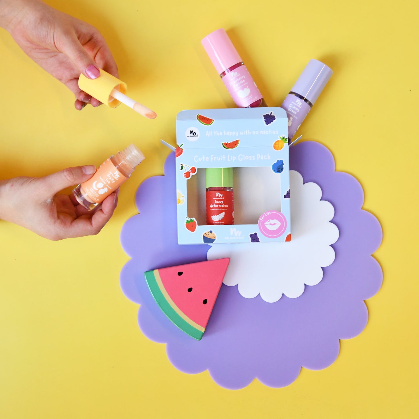 A beauty gift set featuring a 'Cute Strawberry Kiss Pack' by Piyera, displayed on a purple scalloped card over a yellow background. Hands are shown holding two of the lip products (one with a yellow applicator, one with an orange applicator) alongside the boxed set and a watermelon-shaped item.