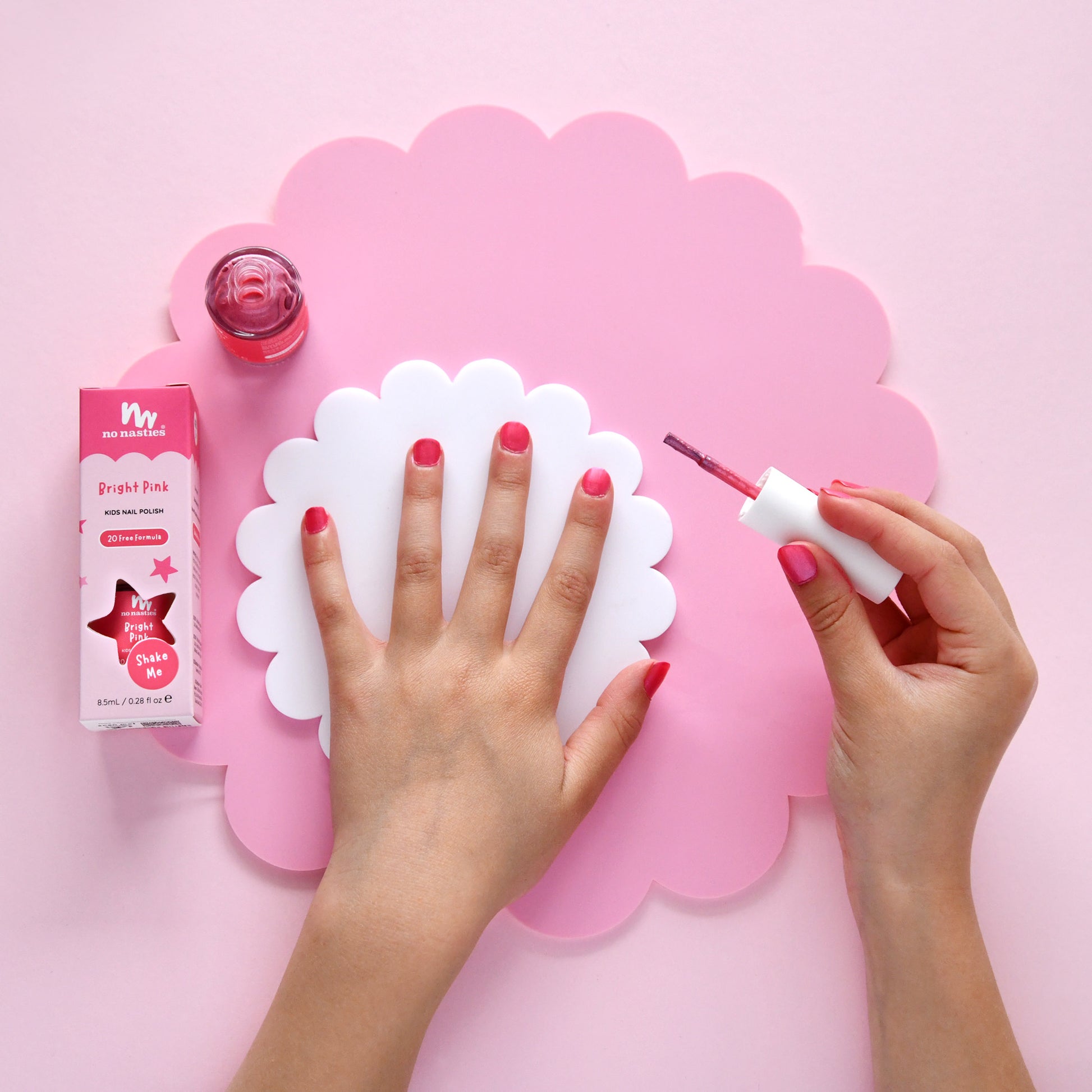 Person applying nail polish with a pink background and nail polish product visible
