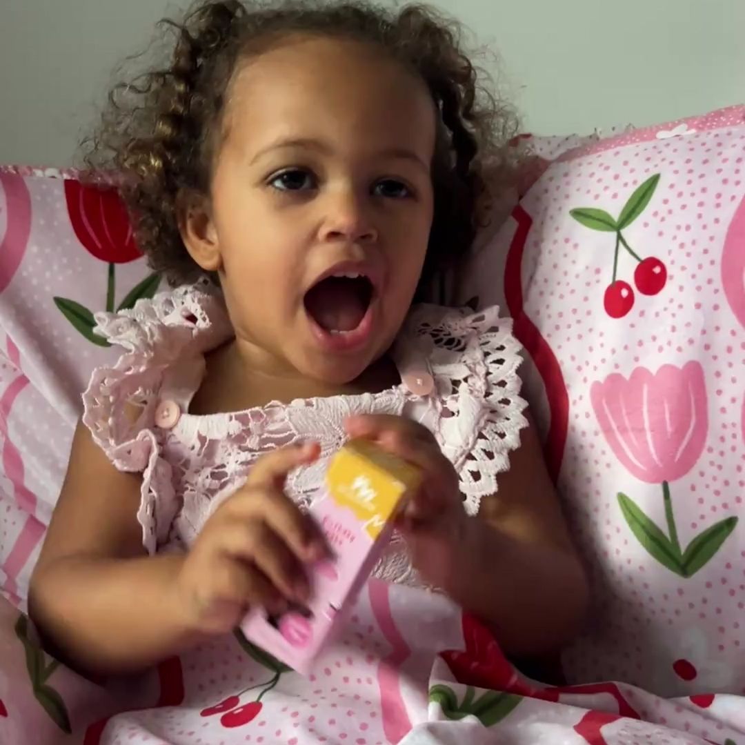 Child in a pink floral dress holding a yellow object on a floral-patterned bedspread.