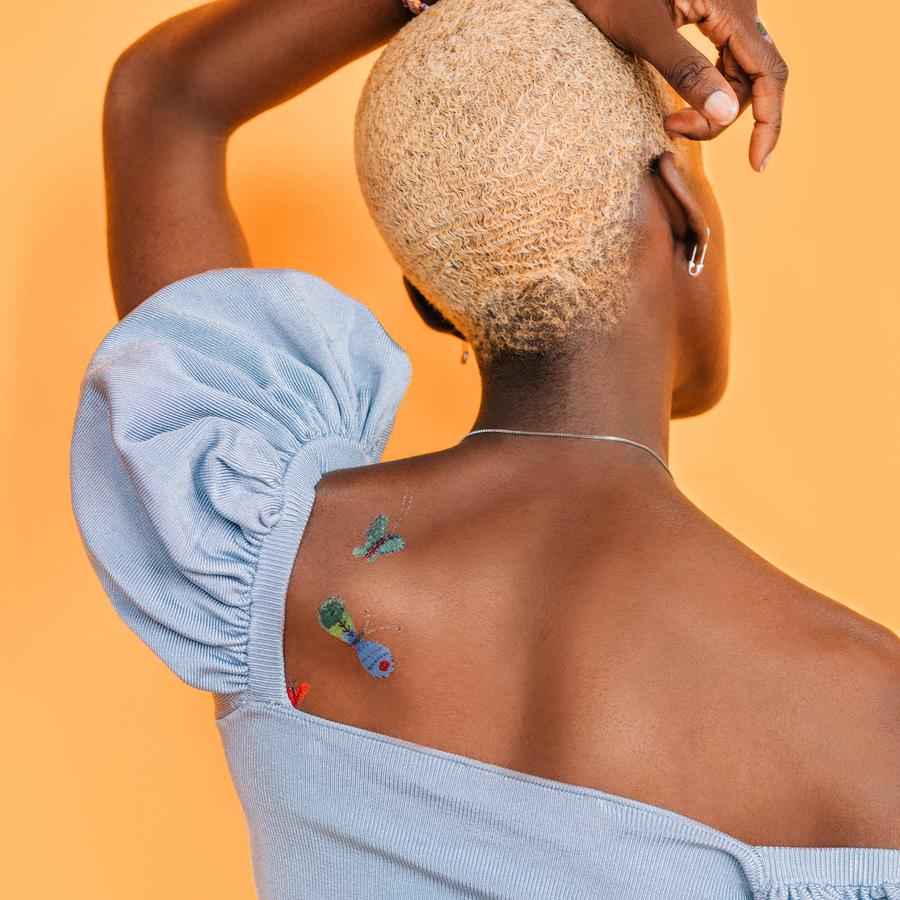 womens-arm-up-with-tattoos-on-shoulder-orange-background