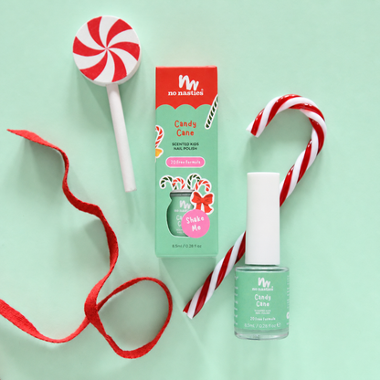 A flat-lay of a nail polish product and its box on a mint green background, styled with candy cane props and a red ribbon. The product is 'Candy Cane' by 'no nonsense' nail polish, in a mint green shade named 'Shake Me'.