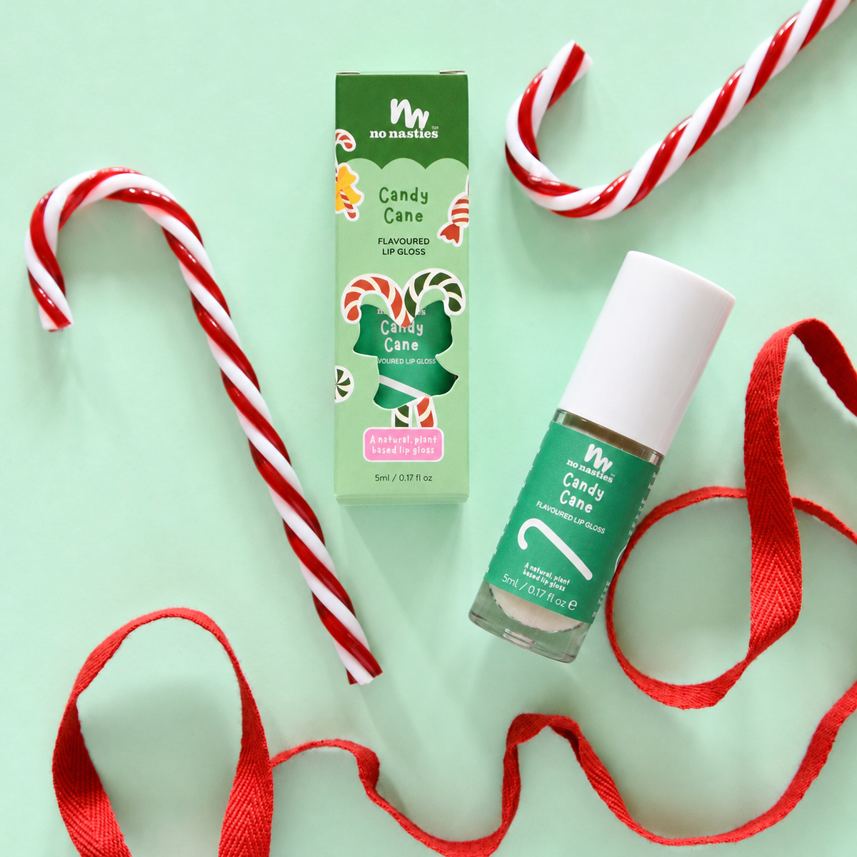 A bottle of lip balm and its green packaging box, both labeled 'W Bio Markers Candy Cane Flavoured Lip Balm', arranged on a mint green background with red-and-white candy canes and red ribbon.