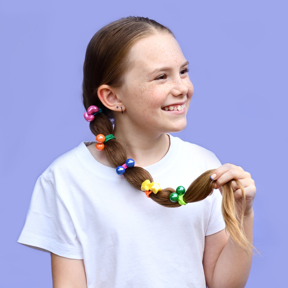 A smiling girl with a ponytail featuring colorful elastic hair ties with star, heart, and ball designs.