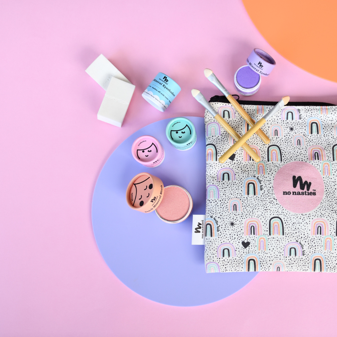 Cosmetic bag with rainbow pattern and 'no nasties' branding, surrounded by various cosmetic items on a colorful background.
