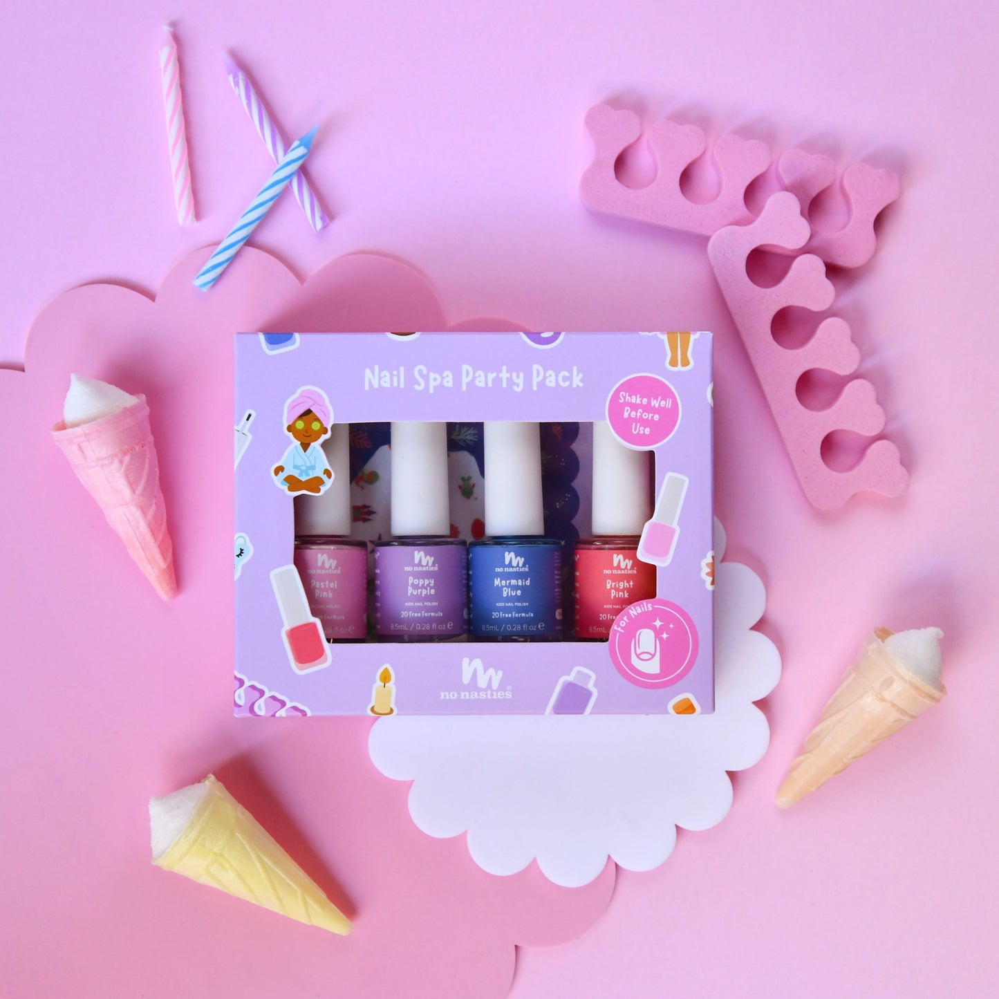 A pink-themed nail spa party pack by Miso Naturals, featuring four nail polish bottles in pink, purple, blue, and red, displayed in a decorative flat-lay with ice cream cones, candles, and pink accessories on a pink background.