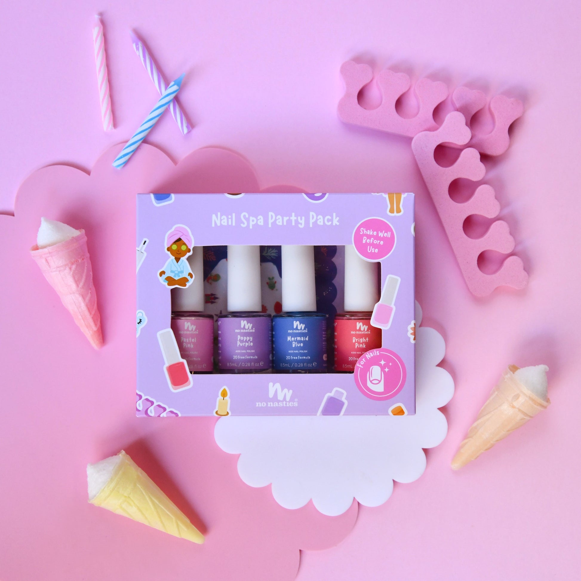 A pink-themed nail spa party pack by Miso Naturals, featuring four nail polish bottles in pink, purple, blue, and red, displayed in a decorative flat-lay with ice cream cones, candles, and pink accessories on a pink background.