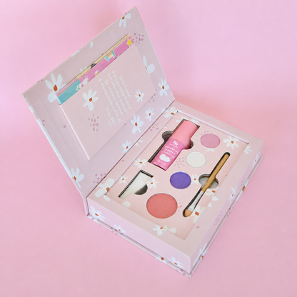 A pink floral makeup gift set in an open box, featuring a pink tube, six round eyeshadow pans in pink, purple, white, and peach, a small brush, and a mirror, all arranged on a soft pink background.