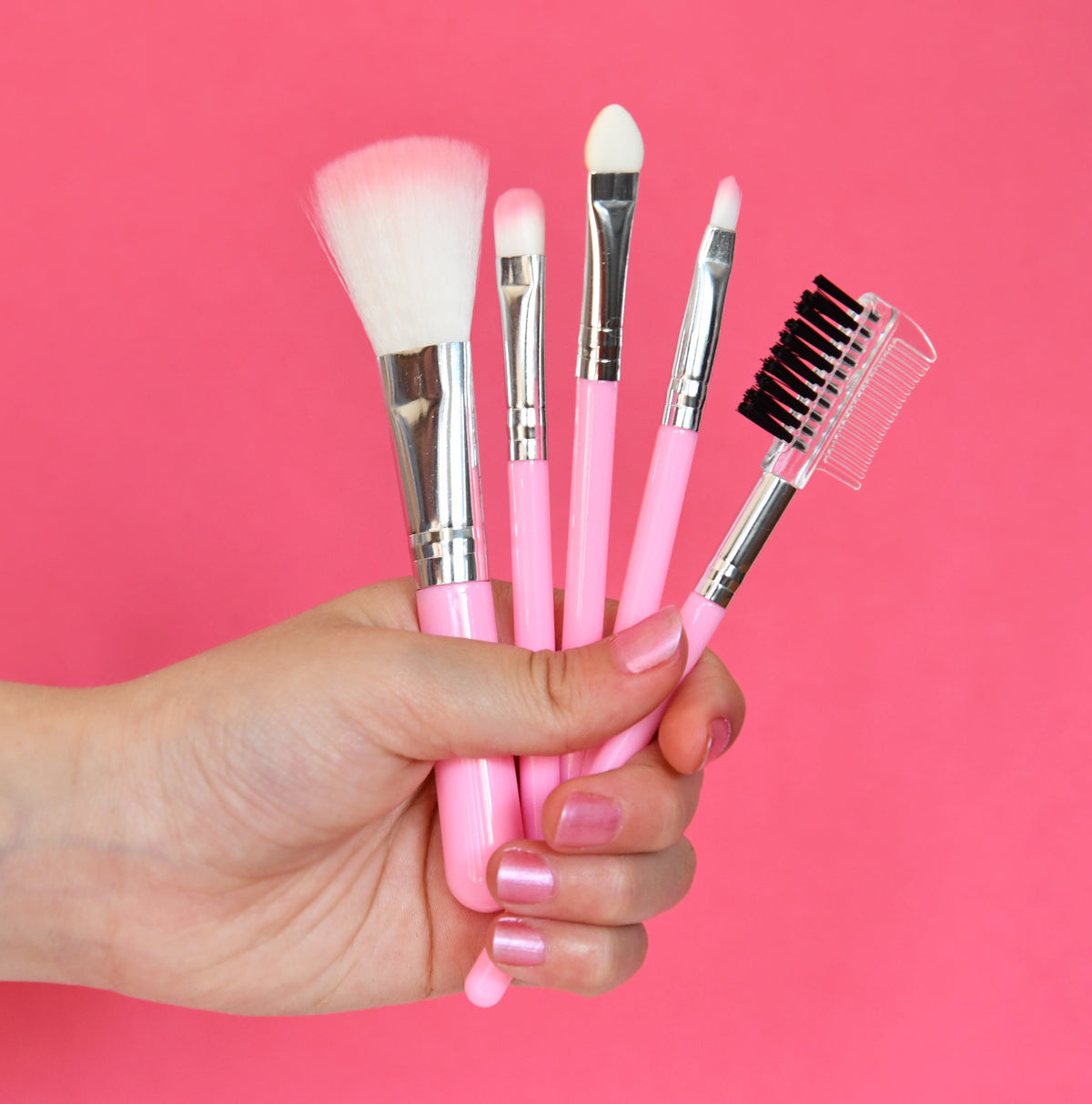 Set of pink makeup brushes held in a hand against a pink background