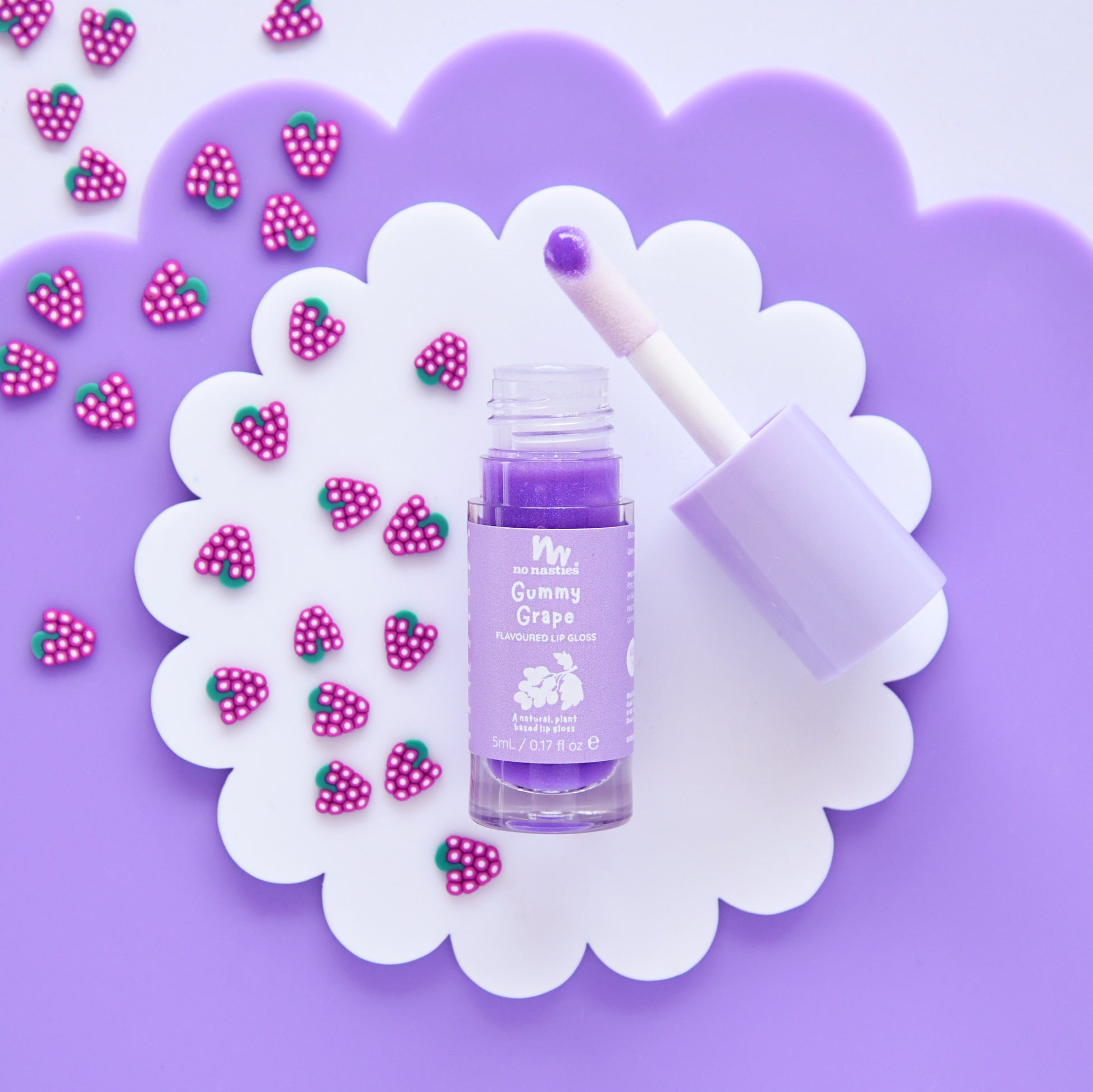 Purple skincare product with a spatula on a decorative white flower with pink strawberry decorations on a purple background