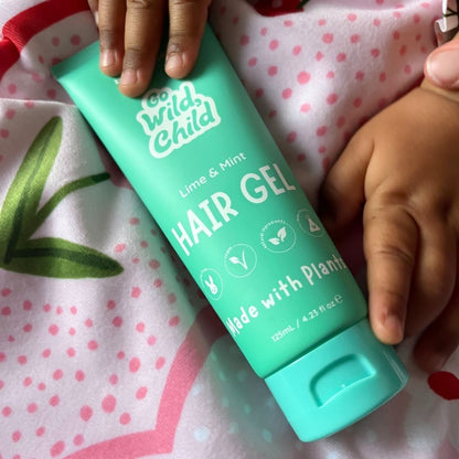 Green hair gel bottle labeled 'Go Wild Child' held by a child's hands on a polka dot fabric background.