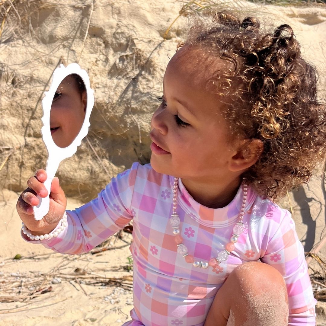 Child holding a small mirror outdoors on sandy ground