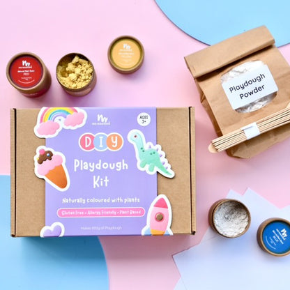 A DIY playdough kit box with various natural colored playdoughs and accessories displayed around it, including containers of powder and spices.