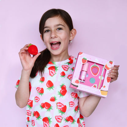 Girl holding a strawberry-themed product set against a pink background