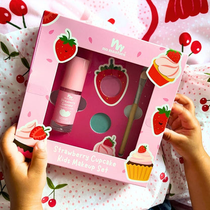 Strawberry-themed kids makeup set in a pink box held by hands on a matching background.