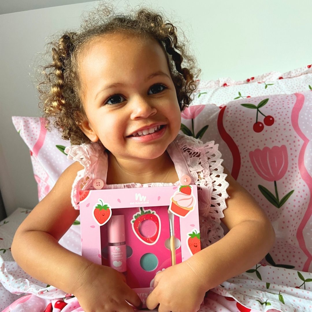 Child holding a pink strawberry-themed gift set on a floral pillow