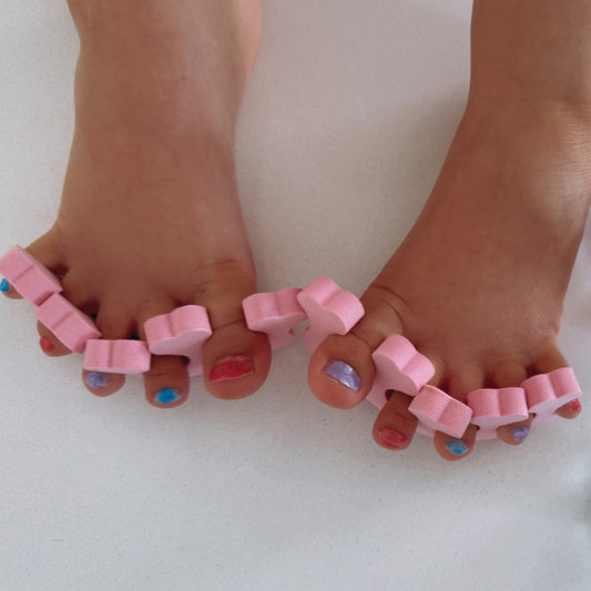 Two pink toe separators designed with heart shapes on the ends, placed on a light green background.